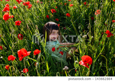 Happy Child Sitting and Playing in a Field of Red Poppies Happy Child Sitting and Playing in a Field of Red Poppies 143662864
