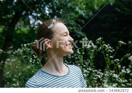 Smiling Woman with Daisies in Her Hair Enjoying Nature in a Garden 143662872