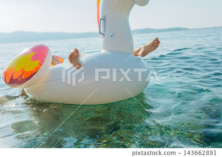 Child feet on inflatable unicorn float in clear sea 143662891