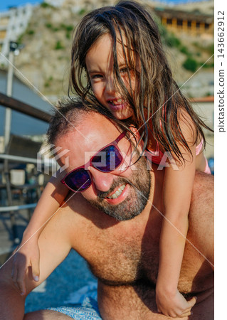 Happy Child Sitting on Her Father's Back on a Beach Summer Vacation Happy Child Sitting on Her Father's Back on a Beach Summer Vacation 143662912