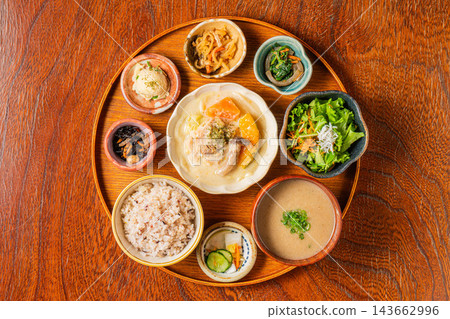 Chicken and vegetable cream stew, a variety of small side dishes, and mixed grain rice served on a round tray. Chicken and vegetable cream stew, a variety of small side dishes, and mixed grain rice served on a round tray. 143662996
