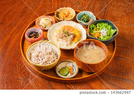 Chicken and vegetable cream stew, a variety of small side dishes, and mixed grain rice served on a round tray. Chicken and vegetable cream stew, a variety of small side dishes, and mixed grain rice served on a round tray. 143662997