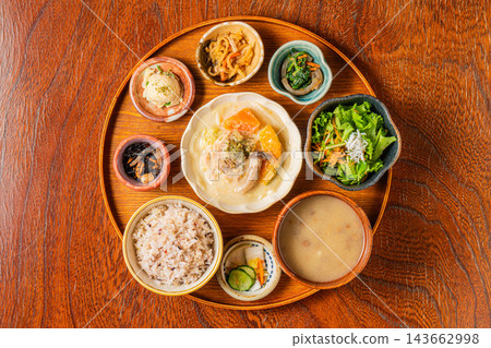 Chicken and vegetable cream stew, a variety of small side dishes, and mixed grain rice served on a round tray. 143662998