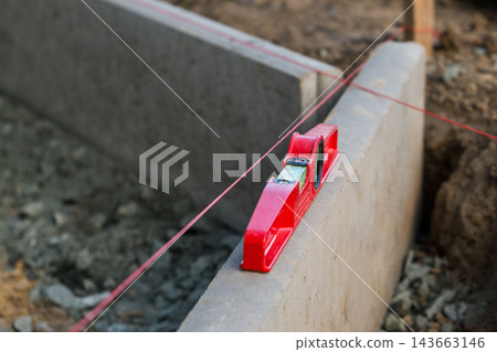 In a construction environment, a leveling tool rests on a concrete block aligned with a string line. In a construction environment, a leveling tool rests on a concrete block aligned with a string line. 143663146