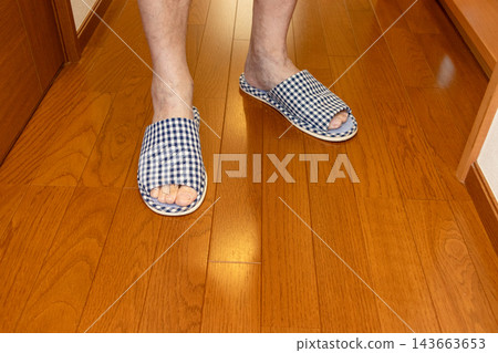 Feet of a person standing on a wooden floor wearing slippers Feet of a person standing on a wooden floor wearing slippers 143663653