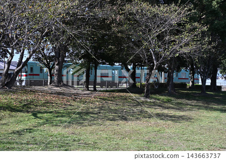 Nishitetsu trains speed past the park, with trees and green lawns in the background. Nishitetsu trains speed past the park, with trees and green lawns in the background. 143663737
