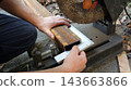 A worker secures a rusty metal pipe in the vise of a chop saw and checks the cutting angle using a metal square. The marking process, which takes place before sawing begins, is carried out outdoors. 143663866