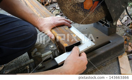 A worker secures a rusty metal pipe in the vise of a chop saw and checks the cutting angle using a metal square. The marking process, which takes place before sawing begins, is carried out outdoors. A worker secures a rusty metal pipe in the vise of a chop saw and checks the cutting angle using a metal square. The marking process, which takes place before sawing begins, is carried out outdoors. 143663866