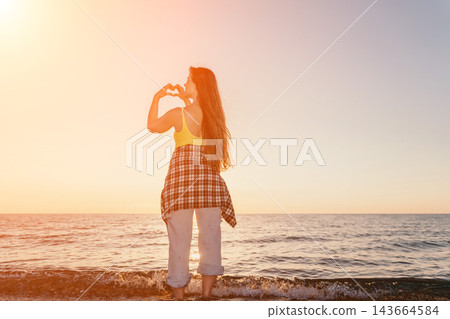 Sunset beach woman making heart shape with hands during golden hour on the sea coast with copy space Sunset beach woman making heart shape with hands during golden hour on the sea coast with copy space 143664584