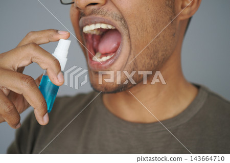 Person using mouth spray in front of gray background Person using mouth spray in front of gray background 143664710