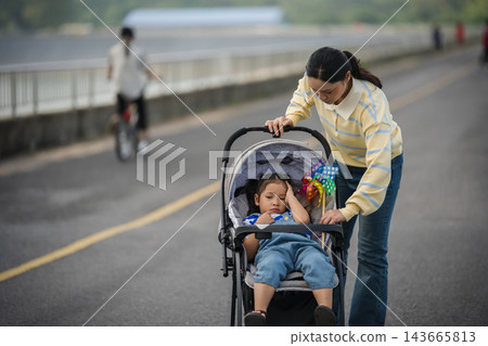mother adjusting stroller shade for sleepy or headache little daughter outdoors on road mother adjusting stroller shade for sleepy or headache little daughter outdoors on road 143665813