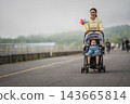 mother walking with child girl sleeping in stroller along the road 143665814