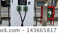 Modern electric vehicle charging station on an urban sidewalk with two cables docked. Glowing green lights indicate readiness for sustainable transit power. 143665817