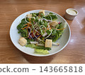 A fresh garden salad with mixed greens, croutons, and sunflower sprouts in a white bowl, served with creamy dressing on a wooden table. 143665818