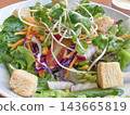 Fresh garden salad served in a white bowl features mixed greens topped with sunflower sprouts, croutons, shredded carrots, red cabbage, and cherry tomatoes for a healthy vegetarian meal. 143665819