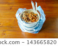 A Korean takeaway food order of spicy meat and rice in paper bowls, packed in a clear plastic bag with chopsticks on a wooden table. Represents food delivery or a convenient office lunch. 143665820