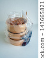 Three brown kraft paper takeout food bowls with clear lids inside a plastic bag on a white background. Includes chopsticks and condiments for a meal delivery or restaurant packaging concept. 143665821