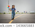 happy preschool child girl walking on road while holding a colorful wind turbine 143665883