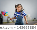 happy preschool child girl walking on road while holding a colorful wind turbine 143665884