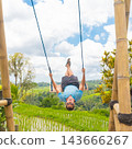 Happy sporty male traveller swinging on wooden swing, enjoying summer vacation in pristine green nature at Jatiluwih rice terraces on Bali, Indonesia. Freedom and life enjoying concept. 143666267