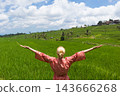 Relaxed fashionable caucasian woman wearing red asian style kimono, arms rised to sky, enjoying pure nature at beautiful green rice fields on Bali island. 143666268