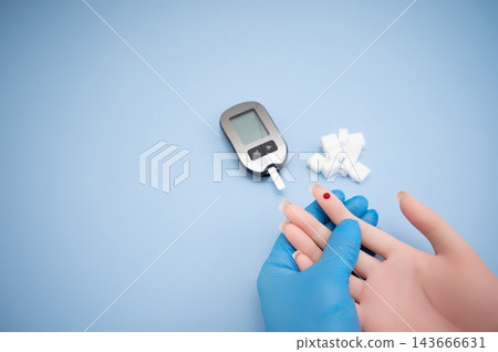 Diabetes concept with blood glucose meter, sugar cubes, blue awareness ribbon and medical gloves on blue background 143666631