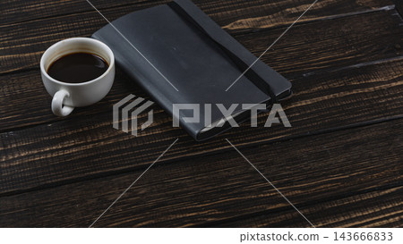 Coffee cup and notebook on a wooden desk during a work break Coffee cup and notebook on a wooden desk during a work break 143666833