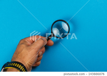 Holding a magnifying glass over a blue background Holding a magnifying glass over a blue background 143666876
