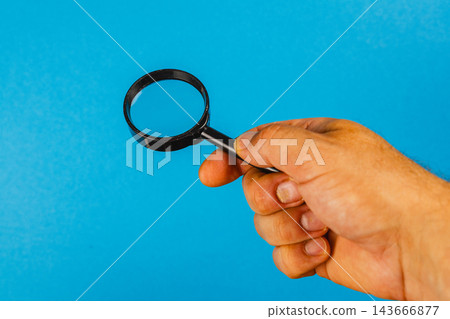 Hand holding a magnifying glass against a blue background Hand holding a magnifying glass against a blue background 143666877