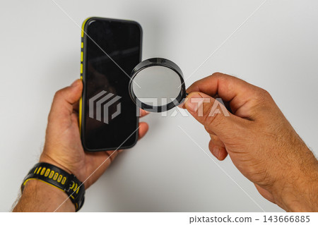 Inspecting smartphone screen with a magnifying glass for details Inspecting smartphone screen with a magnifying glass for details 143666885