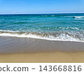 A calm blue sea and a sandy beach with white waves. 143668816