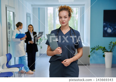 Female doctor in scrubs holding clipboard in modern hospital portrait Female doctor in scrubs holding clipboard in modern hospital portrait 143669343
