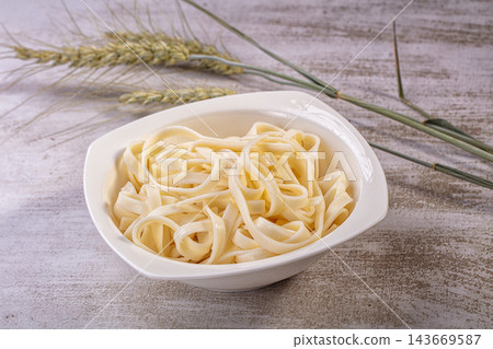 Fresh udon noodles in white bowl with wheat stalks on textured surface Fresh udon noodles in white bowl with wheat stalks on textured surface 143669587