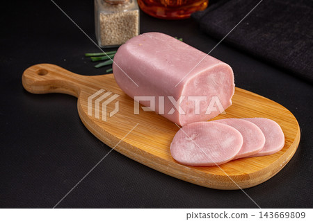 Sliced ham loaf on bamboo serving board with whole pink deli meat block, chives and spices on dark background, deli meat product Sliced ham loaf on bamboo serving board with whole pink deli meat block, chives and spices on dark background, deli meat product 143669809