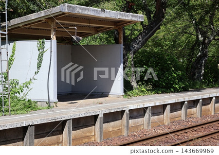 A rural scene of an unmanned train station platform with a small waiting room hut and railway tracks. A rural scene of an unmanned train station platform with a small waiting room hut and railway tracks. 143669969