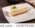 Slice of classic cheesecake with biscuit crust and fresh mint leaf served on white plate over rustic dark wooden table, dessert photography 143670346