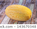Ripe yellow cantaloupe melon with textured rind resting on weathered wooden planks surface 143670348
