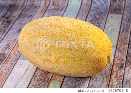 Ripe yellow cantaloupe melon with textured rind resting on weathered wooden planks surface Ripe yellow cantaloupe melon with textured rind resting on weathered wooden planks surface 143670348