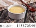 Condensed milk in ceramic white bowl on rustic dark wooden table with brown wooden spoon and striped kitchen towel 143670349