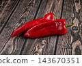 Dark wooden table surface featuring two fresh red ramiro peppers with green stems laid diagonally for vegetarian food ingredient 143670351