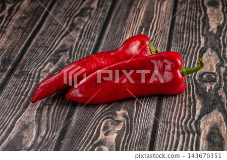 Dark wooden table surface featuring two fresh red ramiro peppers with green stems laid diagonally for vegetarian food ingredient 143670351