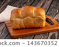 Wooden cutting board, golden brown brioche bread loaf, baked pastry 143670352
