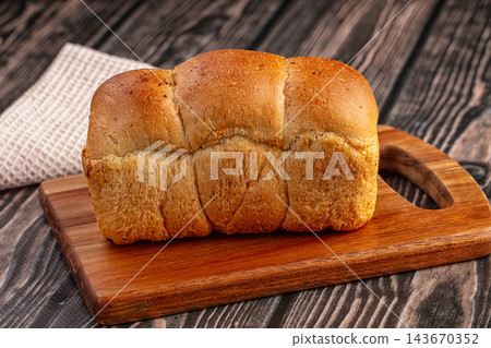 Wooden cutting board, golden brown brioche bread loaf, baked pastry Wooden cutting board, golden brown brioche bread loaf, baked pastry 143670352