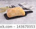 Freshly baked rustic bread loaf on black slate board with wheat ears and checkered napkin on grey stone surface bakery product 143670353