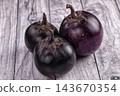 Weathered gray wooden planks background with three round purple eggplants featuring green calyxes and glossy skin, fresh organic vegetable produce 143670354