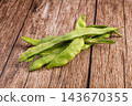 Raw green bean pods scattered on rustic brown wooden table, fresh flat runner beans with natural texture, healthy vegetable food ingredient 143670355