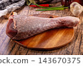 Rustic wooden table surface with raw turkey drumstick on round cutting board surrounded by garlic and chili pepper ingredients 143670375