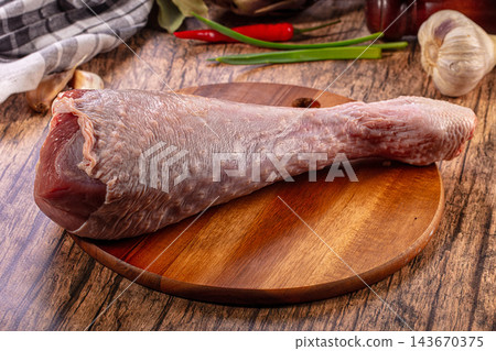 Rustic wooden table surface with raw turkey drumstick on round cutting board surrounded by garlic and chili pepper ingredients Rustic wooden table surface with raw turkey drumstick on round cutting board surrounded by garlic and chili pepper ingredients 143670375