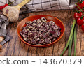 Wooden plate of speckled beans surrounded by garlic, tomatoes and checkered cloth on rustic table, healthy cooking ingredients 143670379