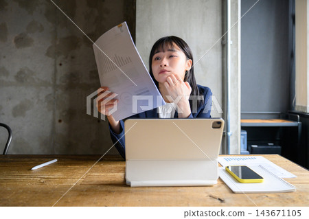 一位女上班族正在認真查看文件上的圖表,陷入沉思。 一位女上班族正在認真查看文件上的圖表,陷入沉思。 143671105